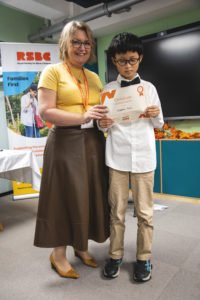 A young boy receiving a certificate standing up next a woman