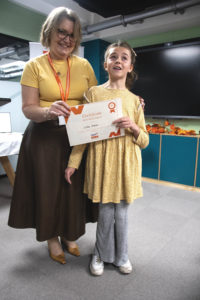 A young girl receiving a certificate standing up next a woman
