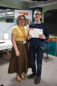 A young boy receiving a certificate standing up next a woman