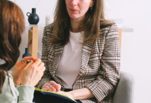 2 women sitting including one listening and taking notes