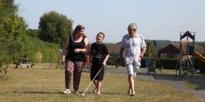 A family walking in a park including a man, a woman and a young boy in the middle with a white cane