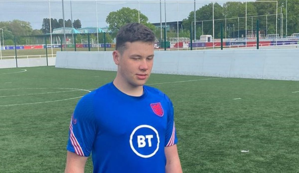 A young man wearing a football outfit standing up in a a football ground