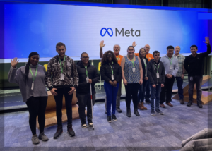 A group of young people and RSBC volunteers standing up in front of a big screen with the Meta logo on it