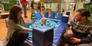 A child playing in a ball pit with his parents next to him.