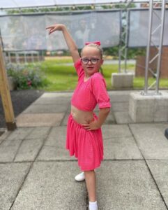 A young girl posing in a pink outfit and looking confident