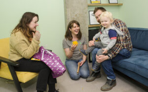 A family sitting in a room with a boy on the lap of his father