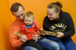A photo of a family with parents playing with their baby boy sitting on the lap of the father and holding music instruments.