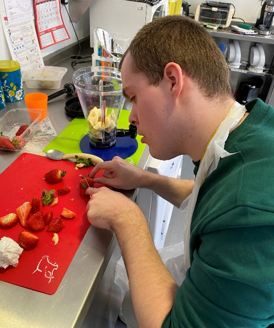 A young man chooping strawberries in a kitchen