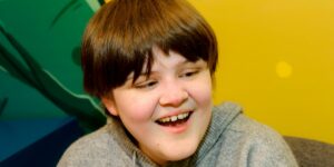 A vision impaired teenager smiling in front of a multicoloured wall.