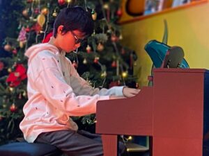 A young man playing piano on with a Christmas tree in the background