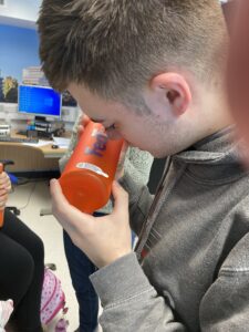 A young person holding an orange water bottle and looking at it closely.