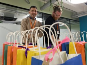 Two young men putting small gifts into a row of brightly coloured gift bags in preparation for an awards ceremony.