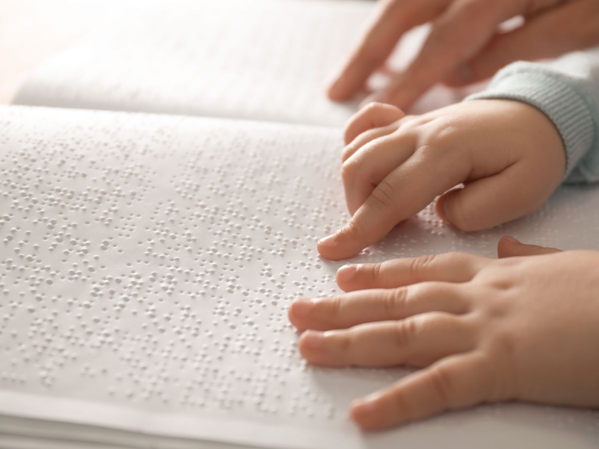 A child's hands are touching a paper Braille book