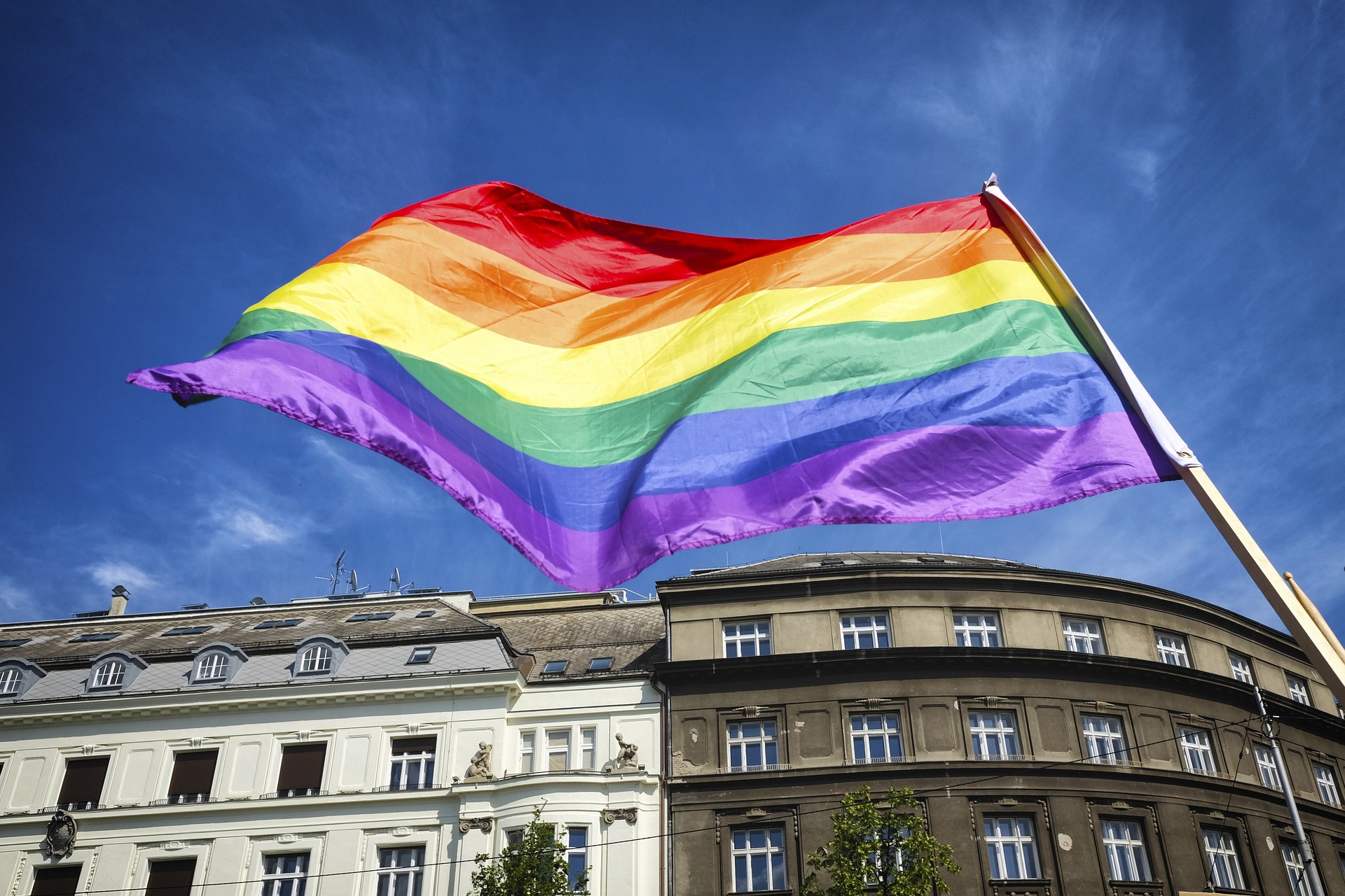 pride flag waving against blue sky and buildings